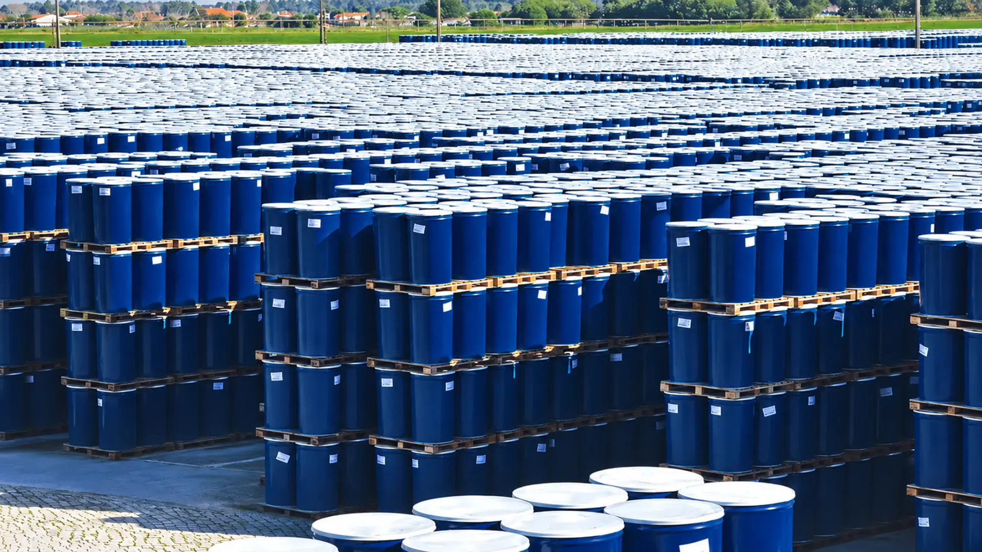 Rows of navy blue steel drums palletized and stacked in an outdoor storage yard